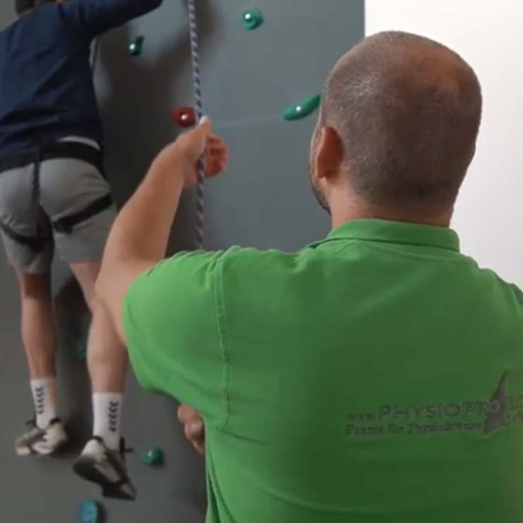 Screenshot 2025-09-25 122832 Physiotherapeut unterstützt Patienten an der Kletterwand bei einer Übung